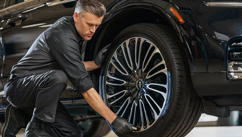 Lincoln technician working on a wheel, performing maintenance or repair with precision tools in a well-equipped service bay.