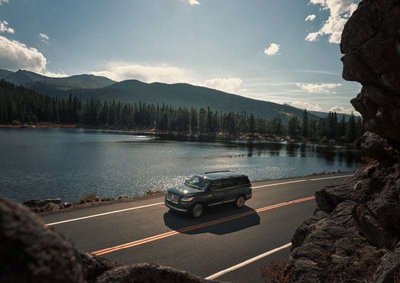 A 2022 Lincoln Navigator SUV is driving along a lake high up in the mountains | Stevens Creek Lincoln in San Jose CA
