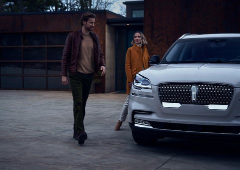 A man and a woman approaching a 2024 Lincoln Aviator® SUV, which illuminates certain lights when they are close | Stevens Creek Lincoln in San Jose CA