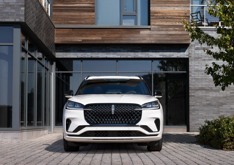 A white 2025 Lincoln Aviator® SUV is shown parked outside a modern building with gray brick and wood accents. | Stevens Creek Lincoln in San Jose CA