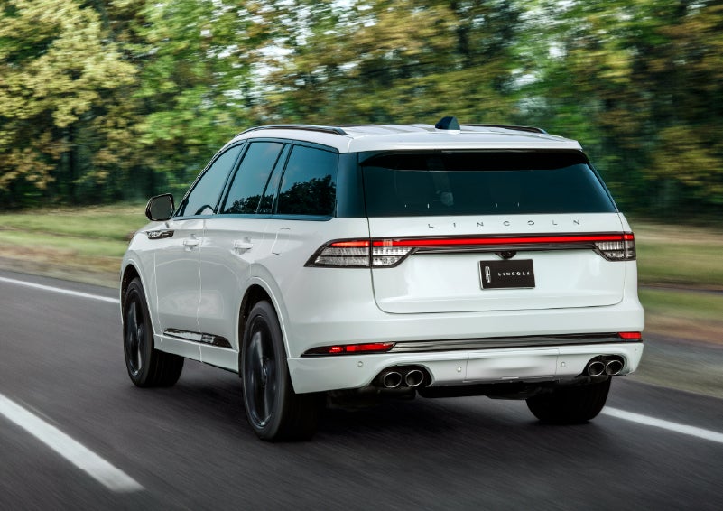 A white 2026 Lincoln Aviator® SUV is being driven away down a road lined with colorful trees. | Stevens Creek Lincoln in San Jose CA