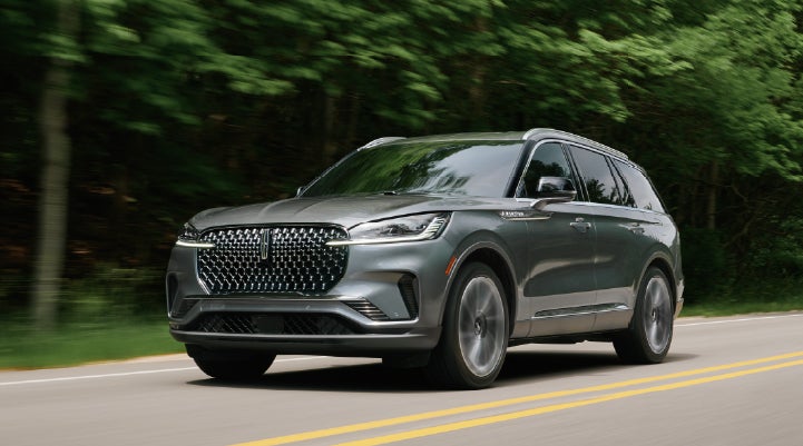 A 2027 Lincoln Aviator® SUV is being driven down a road lined with trees. | Stevens Creek Lincoln in San Jose CA